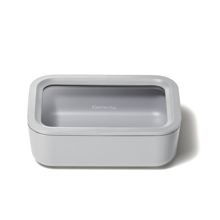 A rectangular, light gray Medium Glass Food Container with Air Release technology and a semi-transparent lid rests against a white background. This non-toxic Caraway container blends style and safety in your kitchen, featuring the brand name on its lid.