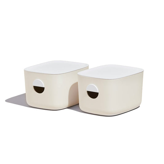 Two Medium Storage Bins from Open Spaces, featuring beige rectangular design and circular handles, elegantly sit on a pantry shelf. With their soft shadows, these bins are perfect for multi-purpose storage.