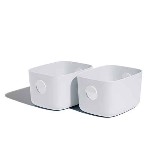 Two Open Spaces Medium Storage Bins, featuring rounded corners and circular handles, are neatly placed side by side on a shelf against a white background. They cast soft shadows to the left, adding an elegant touch of multi-purpose storage.