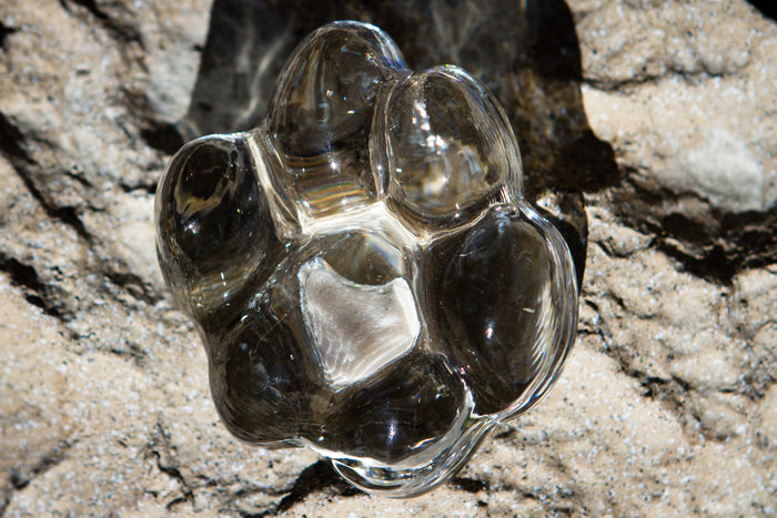 Clear memorial glass paw print keepsake resting on a rocky surface with a white center pad