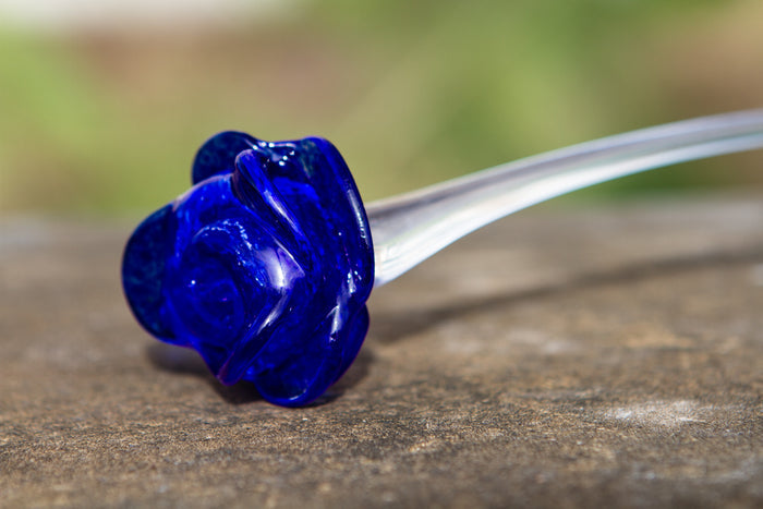 Cobalt blue glass memorial rose with a clear stem resting on a wooden surface