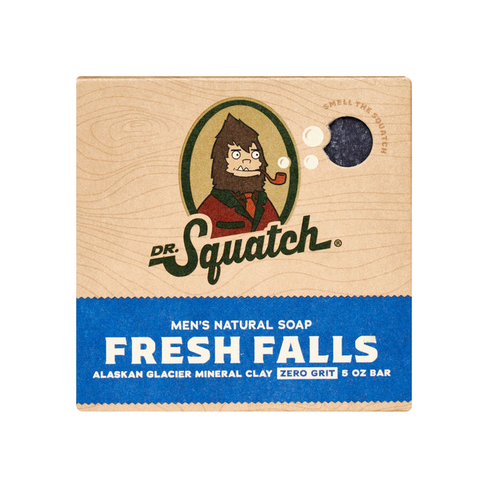 The Dr. Squatch Mens Bar Soap in Fresh Falls scent features packaging with a cartoon character, the text Alaskan Glacier Mineral Clay, Zero Grit, and 5 oz bar. A round window lets you smell the Wood Barrel Bourbon essence mingled with Fresh Falls crisp aroma.