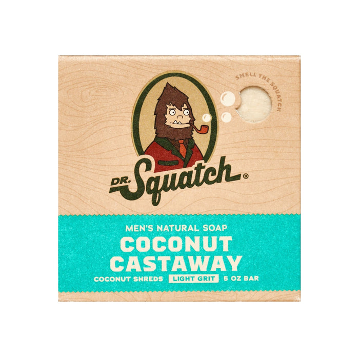The square Dr. Squatch Mens Bar Soap box for Coconut Castaway features a sasquatch illustration. Highlights include coconut shreds, light grit, and a 5 oz bar. A top-right circular cutout states, smell the squatch with a hint of Wood Barrel Bourbon.