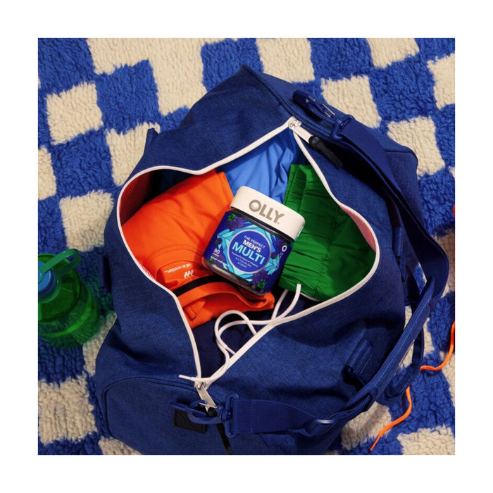A blue gym bag with colorful clothes and a bottle of OLLY Mens Multi vitamins rests on a blue and white checkered surface. A green water bottle peeks out, emphasizing the importance of hydration while the vibrant vitamins energize your day.