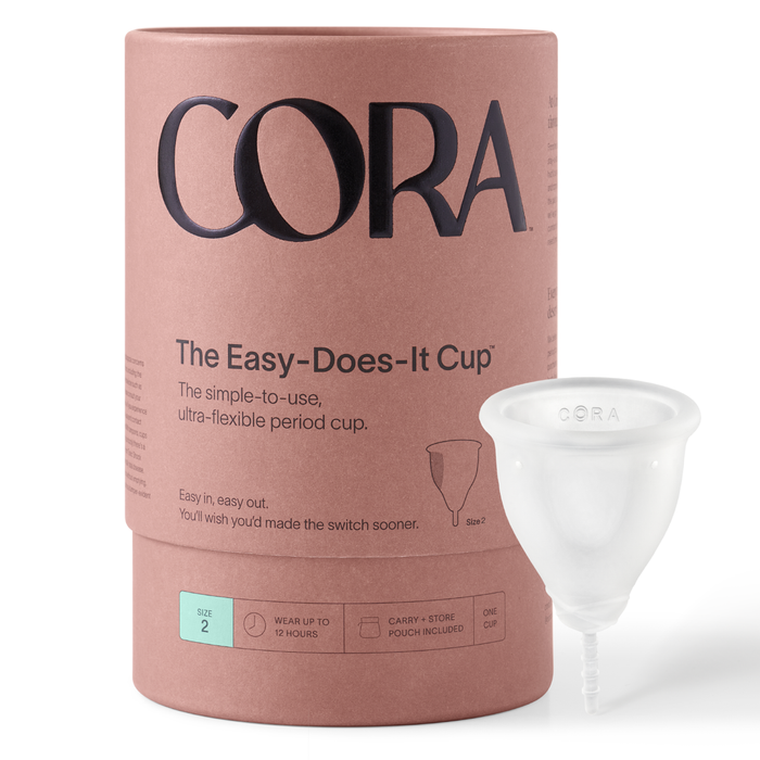 Beside Coras Menstrual Cup packaging is a reusable cup. The box promotes simple-to-use, ultra-flexible, and size 2 features, with text stating: wear up to 12 hours and includes a carry + store pouch. Experience eco-friendly period care with Cora.