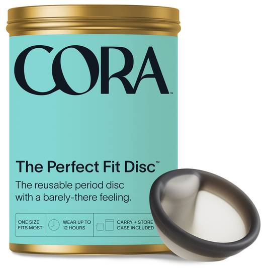 A light turquoise container labeled Cora: The Perfect Fit Disc presents the reusable Cora Menstrual Disc featuring a black rim and white center, offering versatile sizing, up to 12 hours of leak-free protection, and comes with a convenient carry case.
