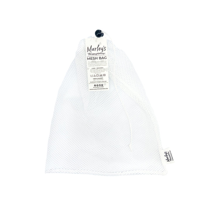 The Mesh Laundry Bag by Marleys Monsters is a white mesh bag with a drawstring closure and black toggle. It includes a tag with product info, icons, and branding. This lightweight, reusable design is ideal for storing UNpaper Towels or serving as a chic laundry bag.