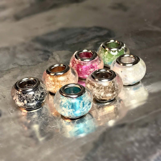 Group of metallic finish cremains beads in blue pink green and other colors on a reflective surface