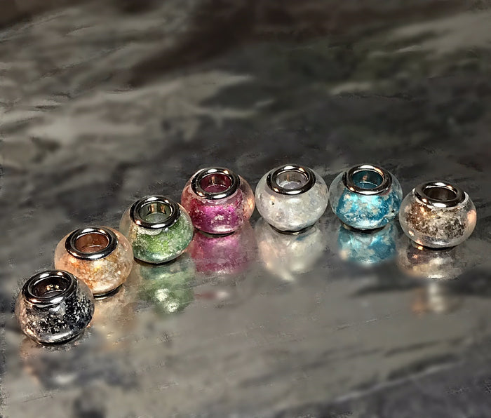 Row of colorful metallic cremation beads with silver rims arranged on a smooth surface