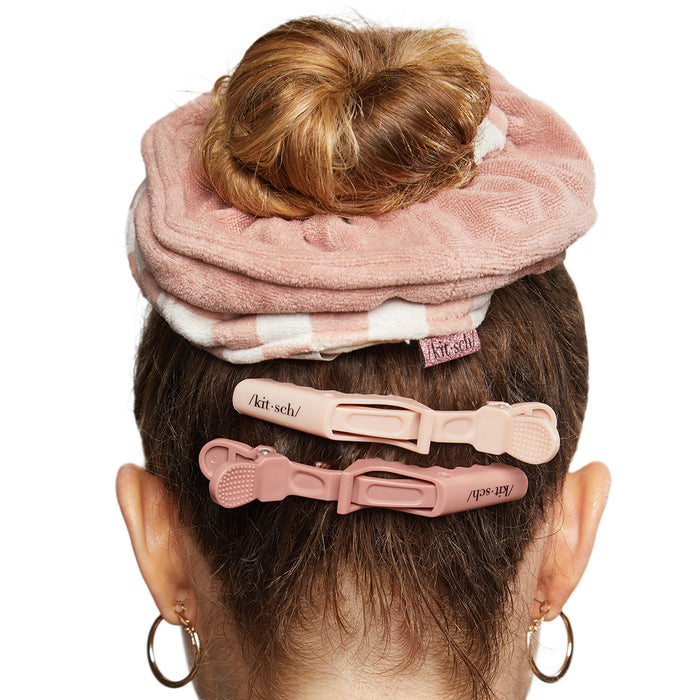 Back view of a person with their hair in a bun, secured by Kitschs Microfiber Quick-Dry Towel Scrunchie and two pink text-decorated hair clips. The smooth brown hair is neatly styled, ideal for post-shower routines. They wear small gold hoop earrings.