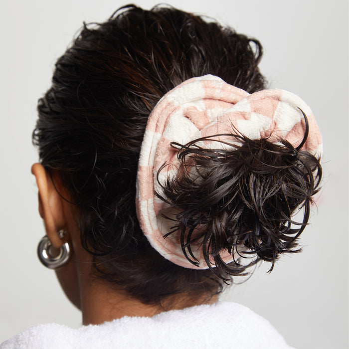 With wet hair in a bun, someone uses Kitschs pink and white Microfiber Quick-Dry Towel Scrunchie, silver hoop earrings, and a white bathrobe, integrating the scrunchie into their post-shower routine, seen from behind.