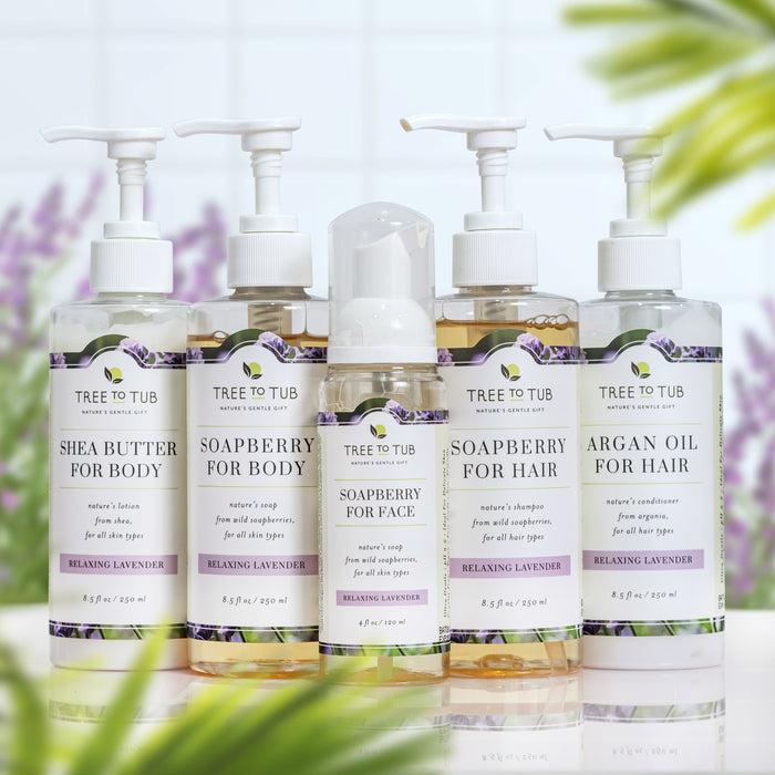 The Tree To Tub lineup includes a Moisturizing Argan Oil Shampoo & Conditioner Starter Set in pump bottles, alongside shea butter and soapberry body and face washes, set against blurred lavender sprigs evoking a soothing scent.