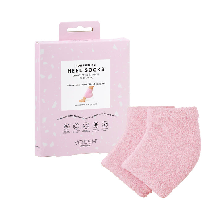 Pink moisturizing heel socks infused with jojoba and olive oil lie next to their speckled light pink packaging, boasting the text Moisturizing Heel Socks, Infused with Jojoba Oil and Olive Oil, while the VOESH New York brand name is prominently displayed.