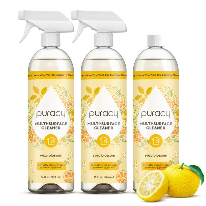 Three Multi-Surface Cleaner Spray bottles with yuzu blossom, beside a sliced yellow yuzu fruit.
