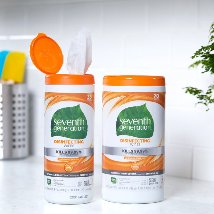 Two Seventh Generation Multi-Surface Disinfecting Wipes containers, featuring an orange lid and label, rest on a kitchen countertop. One container is open with a wipe partially pulled out, set against the charm of kitchen utensils in the background.