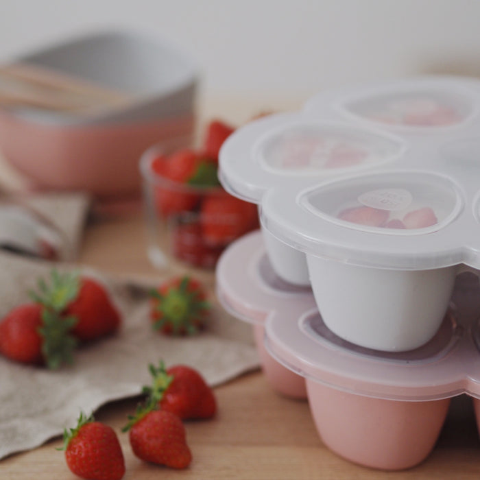 Yogurt cups on a wooden table with fresh strawberries evoke the perfect breakfast scene, while BEABAs Multiportions™ Silicone Baby Food Freezer Tray holds convenient portions of sliced strawberries, complementing meal prep in premium style.
