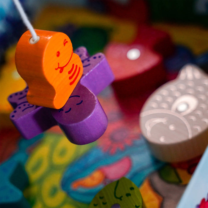 Close-up of vibrant wooden toys, such as an orange face and a purple cross, ideal for enhancing early skills and hand-eye coordination. They create a lively atmosphere similar to My Very First Games - Here, Fishy, Fishy! Magnetic Game by HABA.