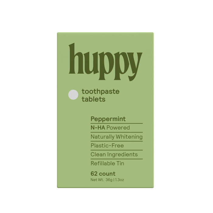 A green box labeled Huppy Toothpaste Tablets with Tin in peppermint, featuring phrases like N-HA Powered, Sustainable Oral Care, Naturally Whitens, Plastic-Free, Clean Ingredients, and Refillable Tin; contains 62 tablets.