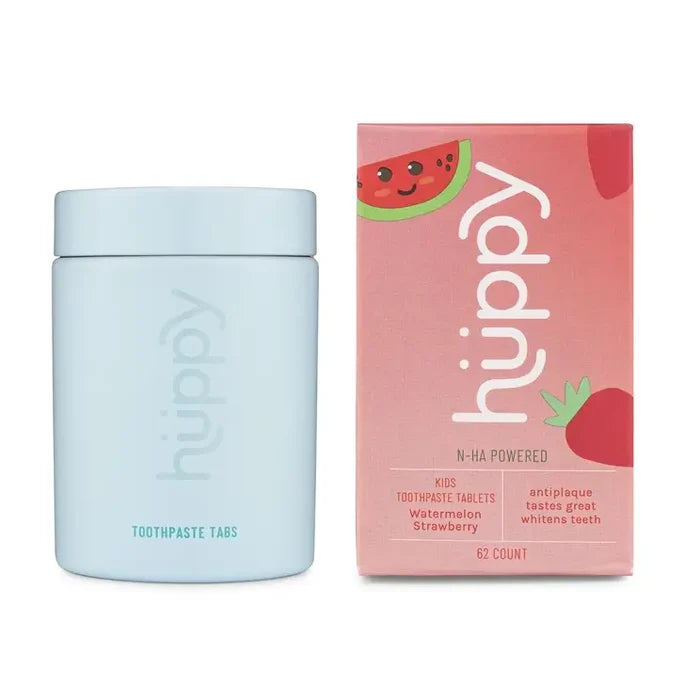 A light blue container of Huppy Toothpaste Tablets stands next to a pink, watermelon-themed box. Packed with N-HA Powered, these sustainable tablets fight cavities and plaque while whitening teeth and offering a refreshing watermelon strawberry flavor.