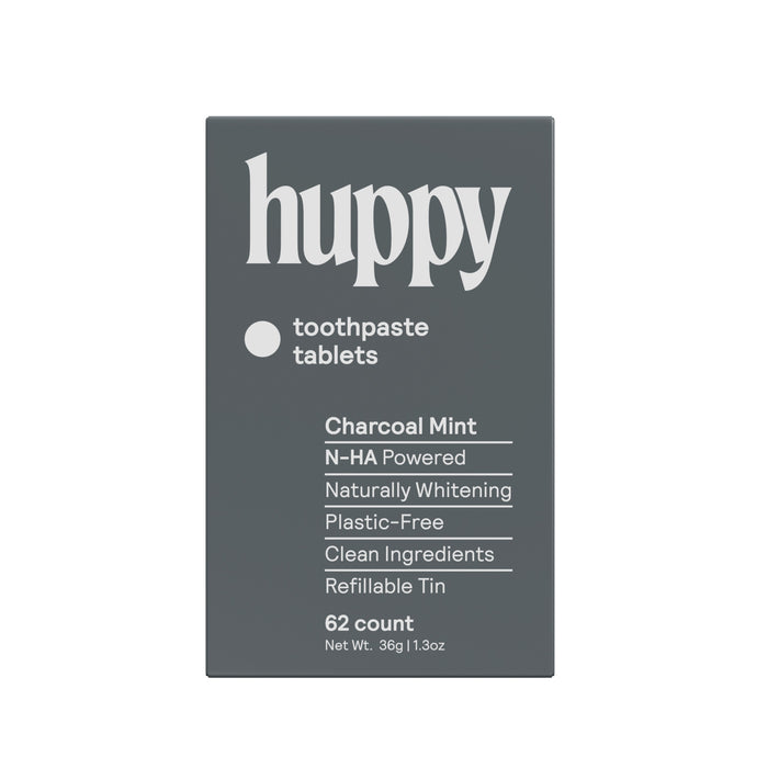 A dark gray Huppy Toothpaste Tablets with Tin in Charcoal Mint, featuring N-HA for cavity protection, natural whitening, clean ingredients, refillable tin, plastic-free packaging, and 62 tablets for a sustainable brushing routine.