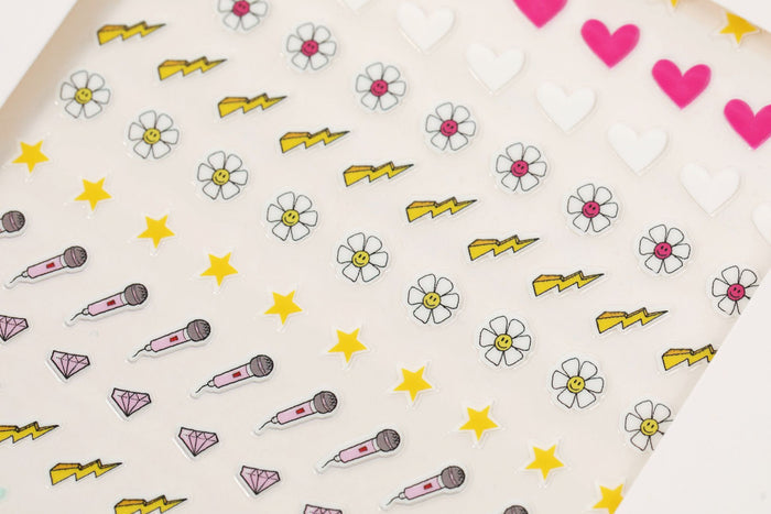 Discover the charming aesthetics of Terra Beauty Bars Nail Art Stickers, featuring pink hearts, white flowers, yellow lightning bolts, stars, microphones, and diamonds on a white backdrop. Pair them with Terra Beauty Bars products for a complete sustainable nail care experience.