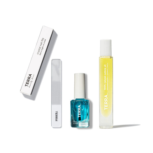 The Nail Boost Growth Kit by Terra Beauty Bars is arranged on a white background, featuring a crystalline nail file, blue nail polish bottle, and yellow cuticle oil for healthier nails. A white box labeled TERRA completes this vegan kit.