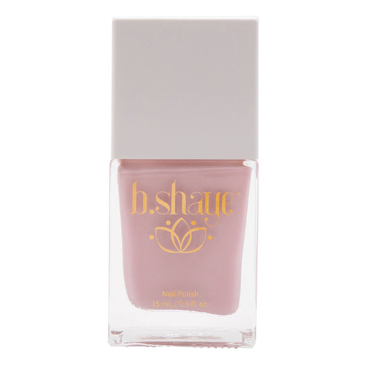 A 15 ml (0.5 fl. oz.) bottle of non-toxic nail polish with pink color is inside a clear container, topped with a square, light gray cap. The label features the brand b.shaye in gold text and a floral design, showcasing this clean beauty product.