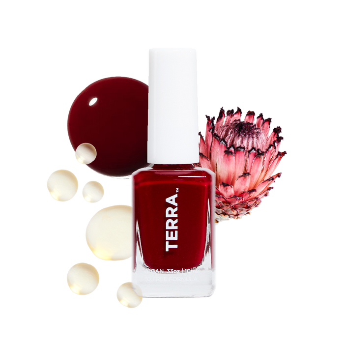 A bottle of Terra Beauty Bars Nail Polish in deep red, a plant-based product, is surrounded by paint drops and a pink protea flower, set against a black background.