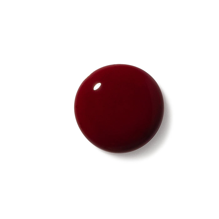 A drop of Terra Beauty Bars deep red vegan Nail Polish on a white background showcases a glossy finish that reflects a highlight, embodying cruelty-free beauty in each bottle.
