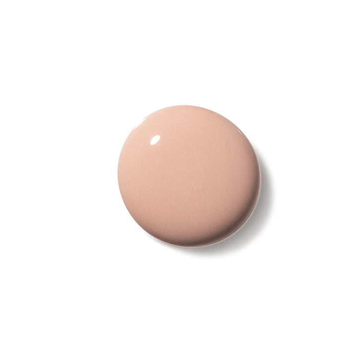 A glossy, nude beige circle of Terra Beauty Bars Nail Polish adorns a white background, its shiny surface capturing the light perfectly. This elegant shade showcases our vegan polishs beauty, being both cruelty-free and plant-based.
