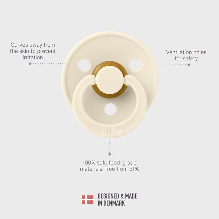 Top view of a cream-colored pacifier with a circular shield. Features include a curved design for skin comfort, ventilation holes for safety, and a ring handle. Made of BPA-free, food-grade materials. Text indicates it's designed and made in Denmark.