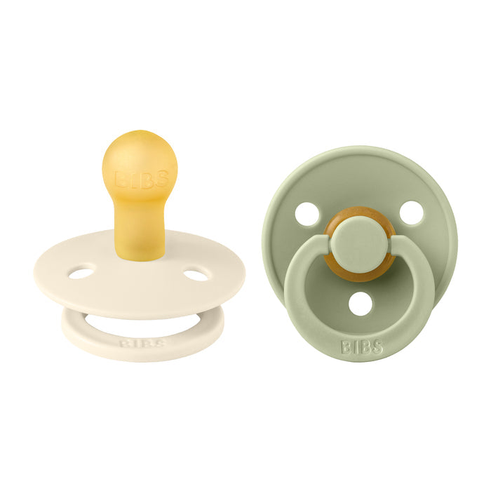 The BIBS Natural Latex Rubber Pacifiers, Size 1 (0-6 Months), are shown in cream with a yellow nipple and sage green. They feature a round shield, two ventilation holes, engraved brand name, are BPA-free, and support breastfeeding.