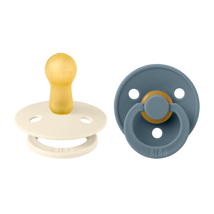 Two BIBS pacifiers are displayed: one has a white base with a yellow natural latex rubber nipple, and the other features a blue base with an orange-rimmed nipple. Both are BPA-free and ideal for breastfeeding support for babies aged 6-18 months.