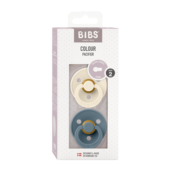 The BIBS Natural Latex Rubber Pacifier, Size 2 (6-18 Months), includes two round pacifiers in cream and teal. Made from natural rubber to support breastfeeding, theyre BPA-free. The white packaging has a dotted pattern and clear plastic window, showcasing quality Danish design.