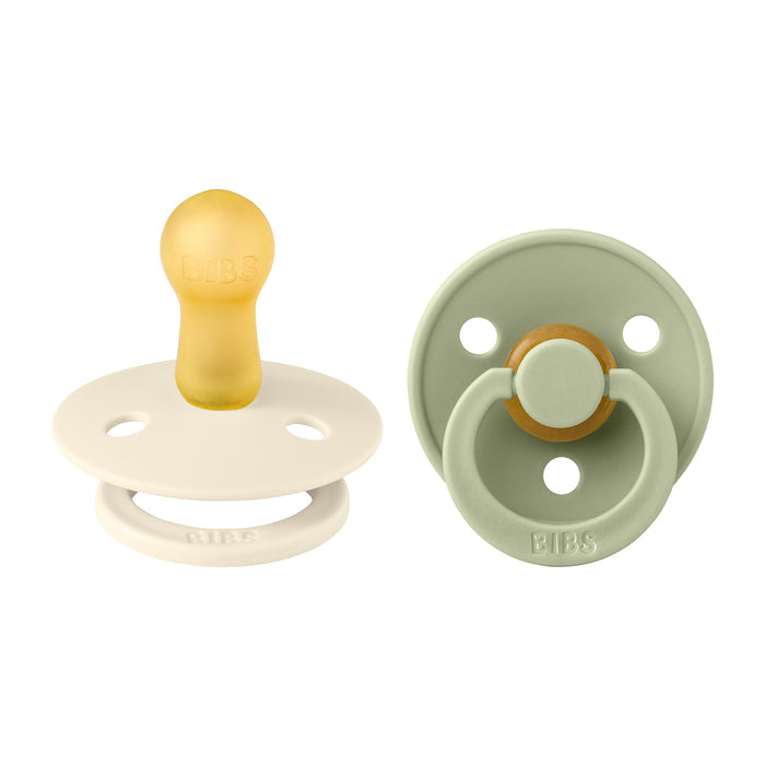 The pacifiers displayed include one with a beige shield and amber nipple, and another with a sage green shield and circular handle. Both round BIBS designs are made from natural latex rubber, BPA free for safe newborn use, fitting size 2 (6-18 months).
