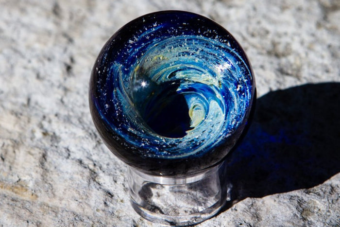 Nightswirl 3D Marble a blue vortex sphere with lighter center and white specks resting on a small clear stand.