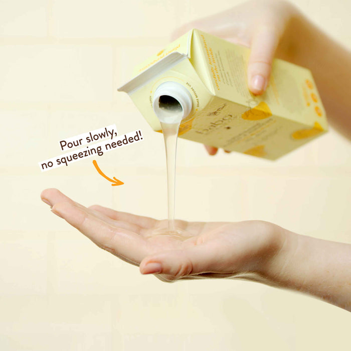 A person pours lotion from a yellow carton onto their open hand. The text on the image reads, "Pour slowly, no squeezing needed!" The background is a soft, neutral color.