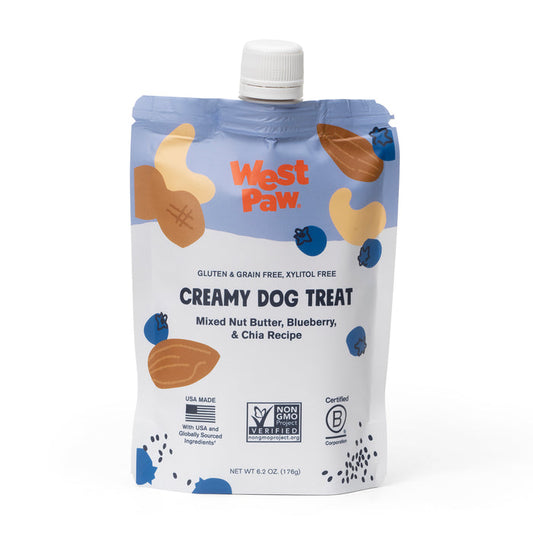 A pouch of West Paw Nut Butter Blueberry Creamy Dog Treat features vibrant graphics of nuts, blueberries, and chia seeds. It highlights plant-based nutrition while being gluten-free, grain-free, xylitol-free, crafted with non-GMO ingredients, and B Corporation certified for quality assurance.