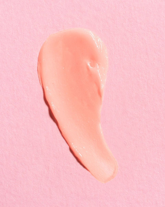 A smooth, swirled smear of light pink cream on a textured pink background resembles the luxurious NYMPH NECTAR Superfruit Radiance Balm by Earth Harbor, inviting tranquility and rejuvenation in just one application.