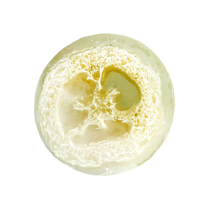 The Oatmeal, Milk & Honey Loofah by Soapymania is a round translucent soap with natural loofah fibers embedded. It features a pale greenish-yellow tint that enhances the intricate loofah webbing for a beautifully textured look.