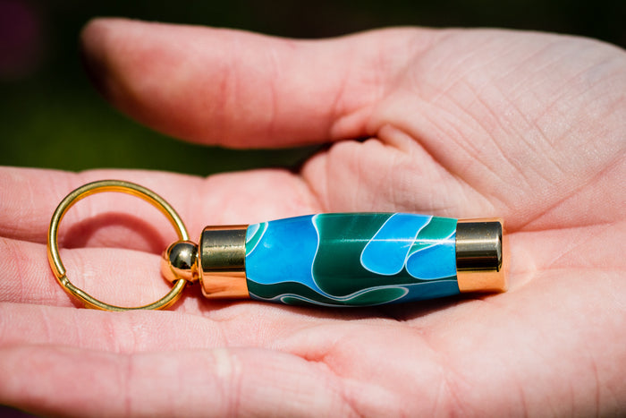 Ocean blue teal acrylic keepsake urn pendant with gold ends and a gold ring, held in a palm