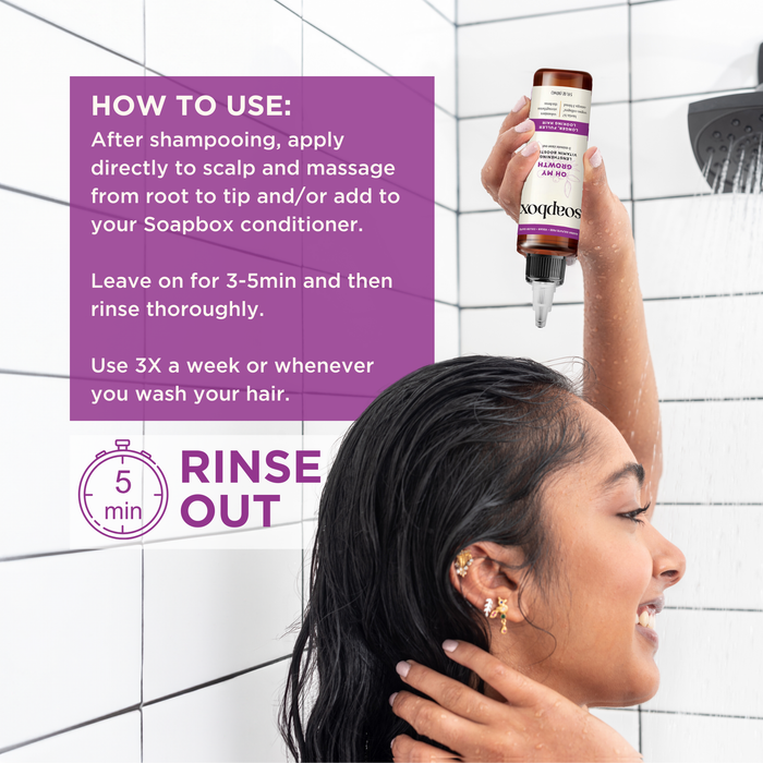 In a shower, a woman with wet hair applies Soapboxs Oh My Growth Lengthening Vitamin Booster Rinse-Out Treatment to her scalp. Instructions: apply after shampooing, leave for 3-5 minutes, rinse. Use 3 times weekly for fuller-looking hair.