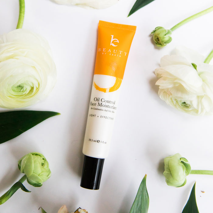 Beauty by Earths Oil Control Facial Moisturizer, in an orange and white tube with a black cap, sits on a white surface among leaves and flowers. It features a light + effective formula enriched with natural ingredients like organic Aloe Vera.