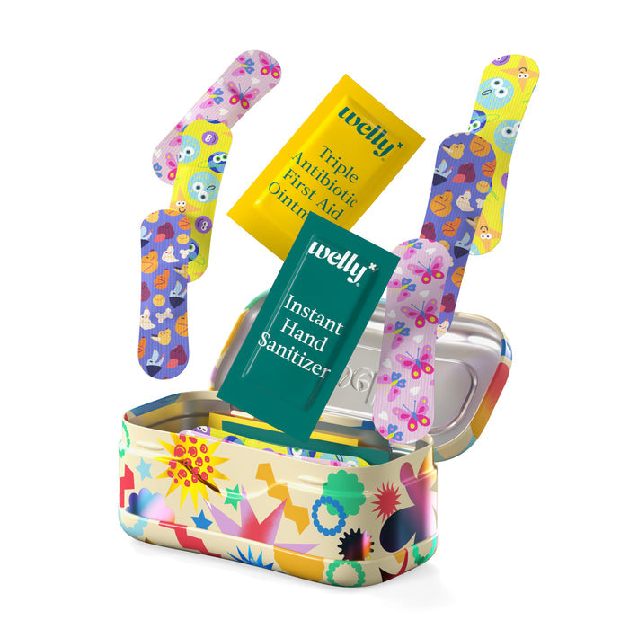 An open Welly On-The-Go First Aid Kit in a colorful, star-patterned tin reveals bright bandages, instant hand sanitizer packets, and triple antibiotic ointment.