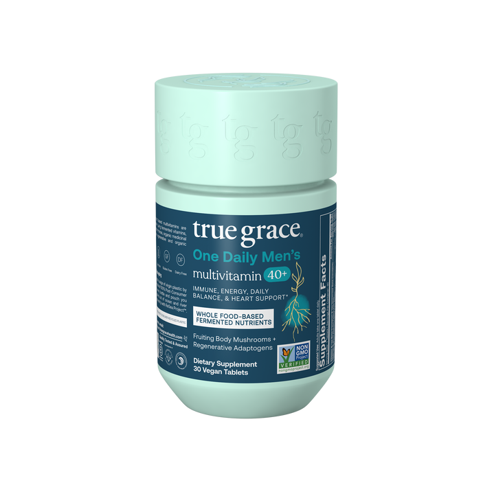 A teal bottle of True Grace One Daily Mens 40+ Multivitamin with labels highlighting immune, energy, heart support, daily balance, vegan tablets, whole food-based nutrients, chelated minerals, and non-GMO certification.