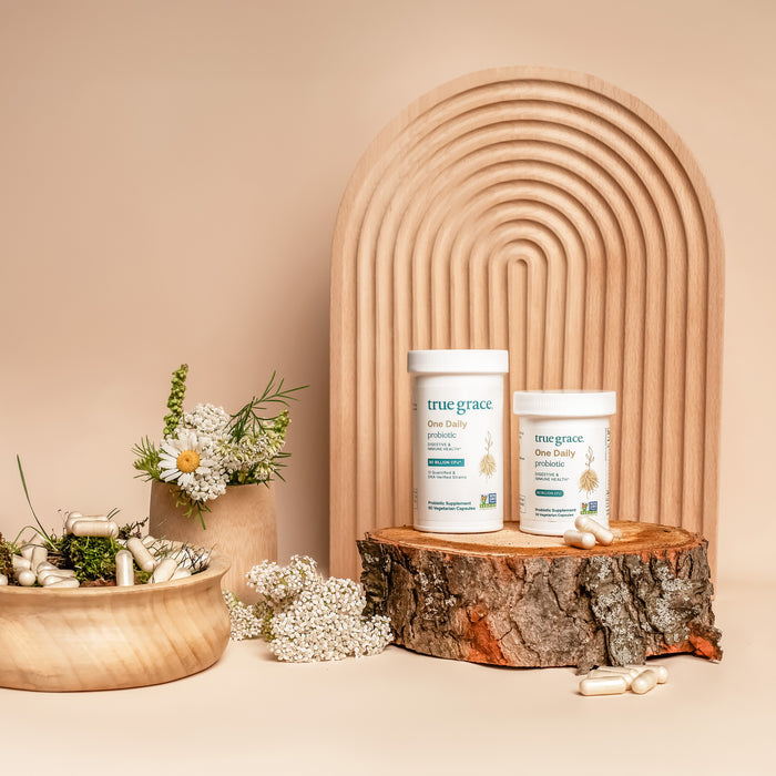 Supplement containers on a wooden pedestal with bark, surrounded by white capsules and small floral arrangements. The background features an arch decor piece and beige tones for an earthy, natural look.