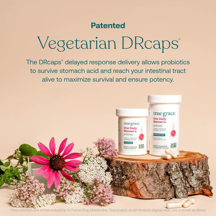 Two True Grace One Daily Women's Probiotic bottles rest on a wooden surface with assorted flowers, highlighting patented Vegetarian DRcaps, probiotics, and prebiotic fiber for digestive, vaginal, and immune health benefits.