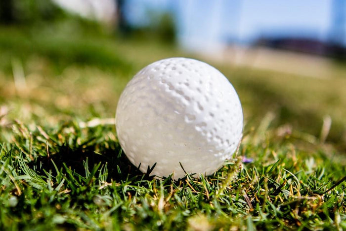 Opaque glass golf ball infused with cremation ash resting on grass in bright outdoor light