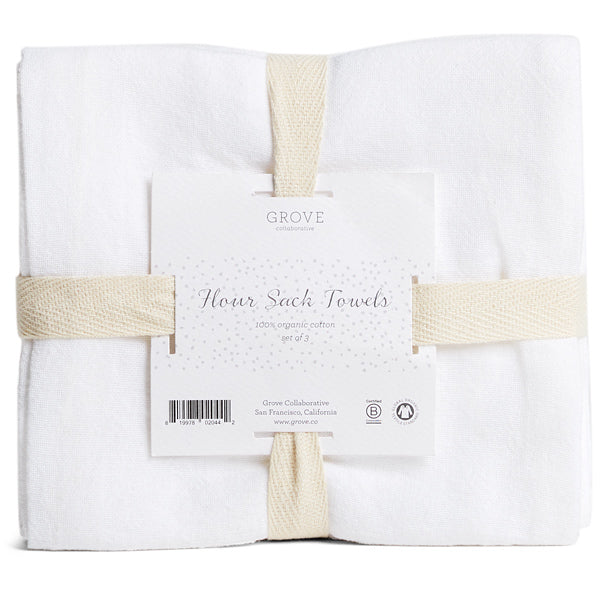 A set of three white Organic Cotton Flour Sack Towels by Grove Co., made from 100% organic cotton, ideal for kitchen use, wrapped with beige straps and labeled Grove Collaborative.