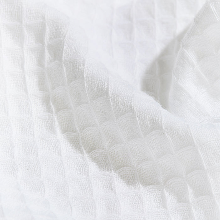 A close-up shows the Grove Co. Organic Cotton Hair Towels white textured fabric with a waffle weave pattern. Its grid-like design of raised squares creates a soft, cozy look, making it perfect for gentle use. Subtle folds and shadows enhance its gently draped appearance.
